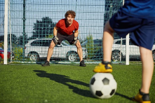 Father goal keeper and boy son forward training football at stadium. Active family having fun outdoors enjoying sport leisure time
