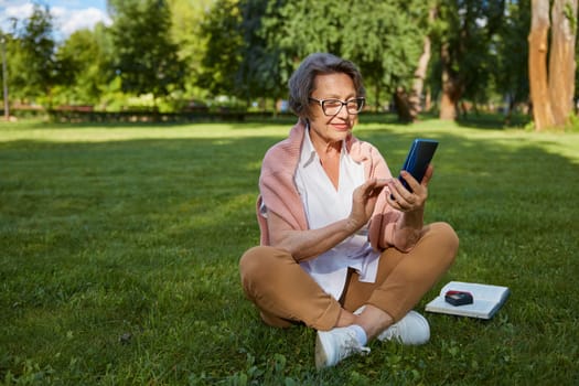 Senior businesswoman using mobile phone to solve problem or making call while rest in park during break time
