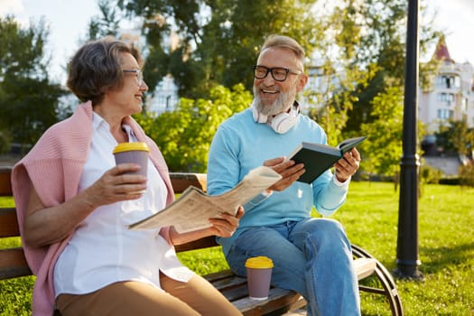 Concentrated man and woman couple reading on city park bench. Happy retirement and free weekend time
