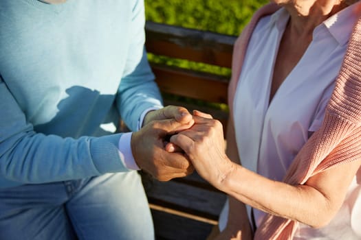 Closeup view of senior couple hands in hands together. Old man and woman giving love, support and empathy each other. Romantic date and walk for elderly people in public park