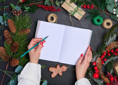 A woman sits at a table surrounded by Christmas decorations and gifts. She writes in a notepad, top view