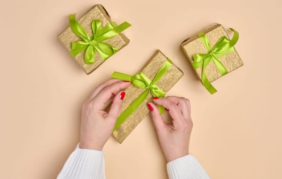 Female hands holding a gift box with a green ribbon on a beige background. View from above