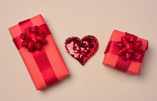 Red heart and boxes packed in red paper and tied with ribbon on a beige background, gifts