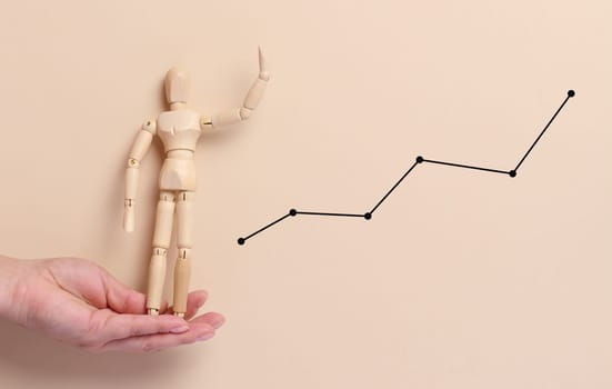 Female hand holding a wooden mannequin on a beige background with a graph