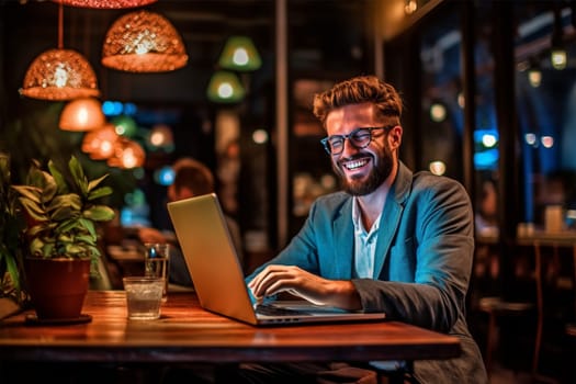 A young man works at a laptop in a cafe and smiles.