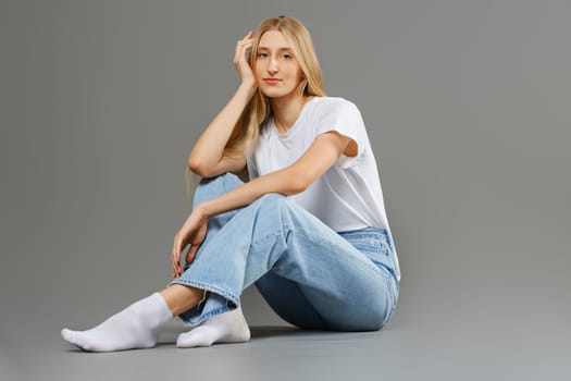 A bored woman sits on the floor with her head propped up on her hand and her legs crossed