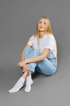 Thoughtful and calm woman sitting on the floor cross-legged on grey background