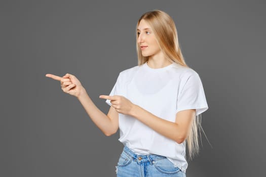 Young blonde woman wearing jeans and shirt pointing to the side with both index fingers