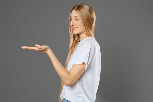 Nice woman stretched her hand forward with her palm up and looks at it with a cute smile