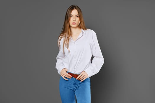 Studio portrait of young woman in white shirt, blue jeans on grey background