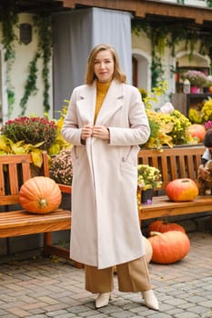 Stylish woman in beige coat and wide trousers at autumn pumpkin fair