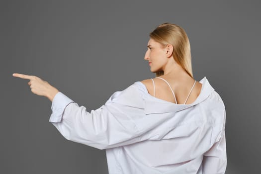 Back side view of woman wearing white shirt pointing to the side with index finger