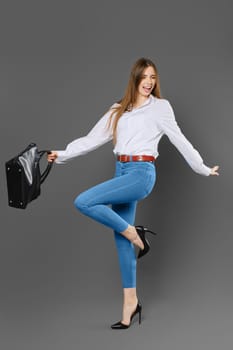 Joyful woman waving her arms while holding a bag and standing on one leg