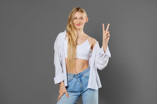 Happy woman showing victory sign on grey studio background