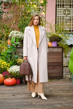 Cute woman in coat, loose trousers and boots at autumn fair