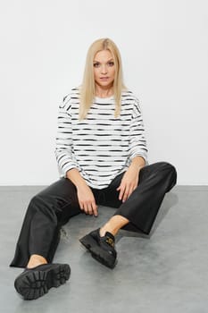 Fashion model in a striped blazer and wide leather pants sits on the floor