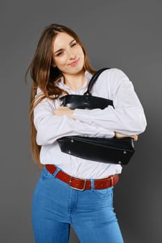 Playful young woman hugs her bag and grimaces on grey background