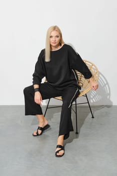 Portrait of blonde woman in loose casual clothes and leather sandals on a wicker chair