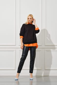 Blonde woman in leather pants and a shirt sticking out from under a sweater