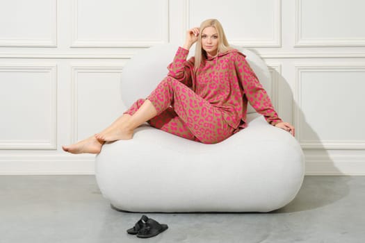 Barefoot woman in a warm home clothes sits in profile in a bright room