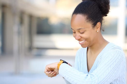 Black woman checking smartwatch smiling in the street