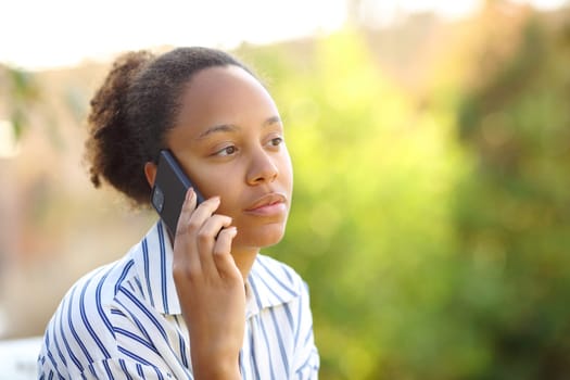 Black woman talking on phone on green in a park
