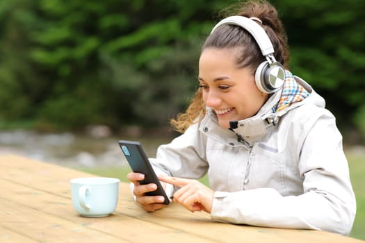 Happy hiker listening to music with headphones and smart phone in a picnic table