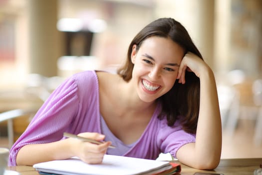 Happy student laughing looking at you in a bar terrace