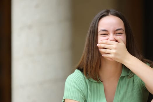 Happy woman laughing covering mouth looks at you in the street