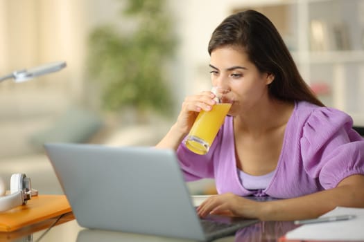 Student e-learning using laptop drinking orange juice at home