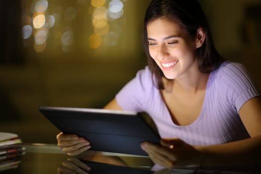 Happy woman watching media on tablet at night at home