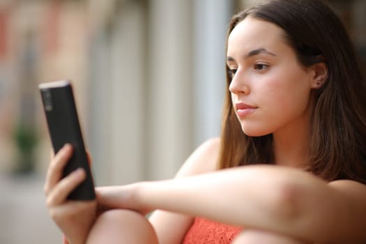 Serious woman checking phone content outdoors in the street