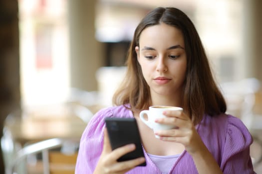 Front view portrait of a serious woman checking phone drinking in a bar terrace