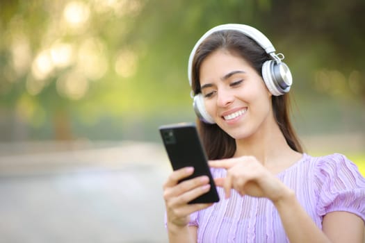 Happy woman listening to music using headphone and smart phone in a park