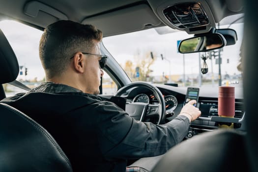 A man uses a smartphone installed in the holder while driving a car.