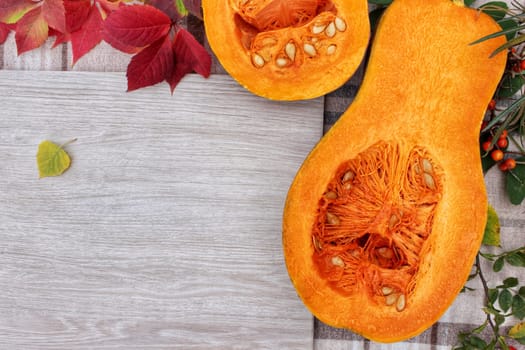 checkered beige autumn background with edible cut pumpkin and crimson yellow leaves.