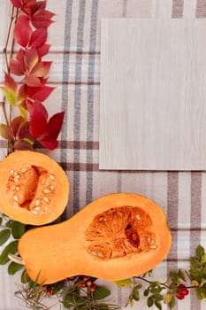 checkered beige autumn background with edible cut pumpkin and crimson yellow leaves.