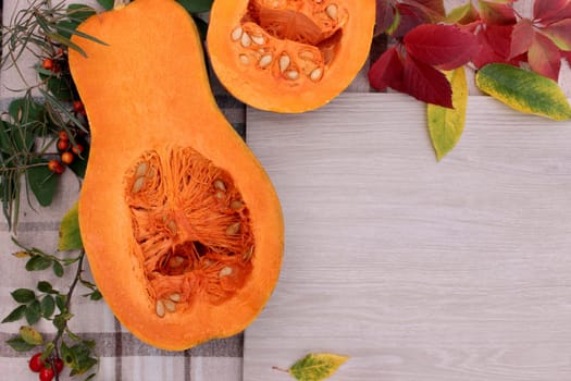 checkered beige autumn background with edible cut pumpkin and crimson yellow leaves.