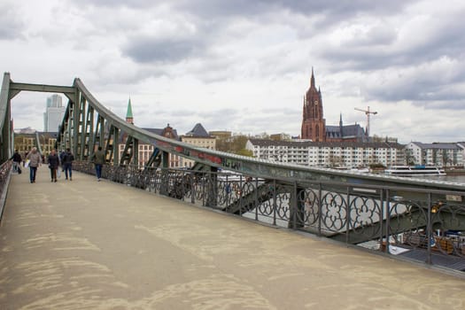 Frankfurt am Main, Germany. / April 26 2023 :  people enjoy crossing river Main at the Eiserner Steg in Frankfurt. The bridge from 1868 is for pedestrians only.