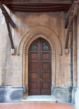 Close-up of a weathered wooden door in a brick wall. The door has a metal handle and a stained glass window in the upper part. The brick wall has a few cracks