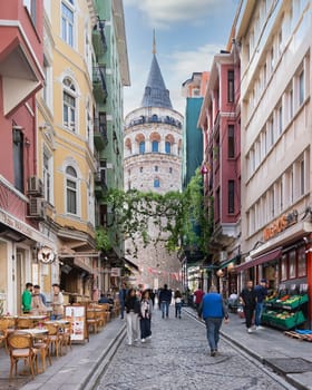 Istanbul, Turkey - May 13, 2023: Popular tourist destination Galata Tower, taken from the narrow and atmospheric cobblestone crowded Buyuk Hendek Street