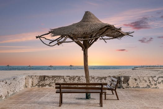 Relaxing sunset at the beach with wooden benches and a ruined thatched umbrella