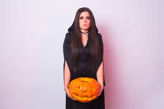 Young woman in Halloween witch costume in studio with yellow pumpkin