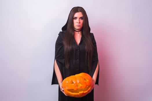 Woman as witch is standing with the pumpkin in the studio. Halloween and carnival concept.