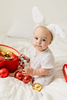 Christmas Baby in Santa Hat Child playing with baubles. Present Gift Box over Holiday Lights background and Merry Christmas