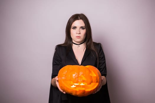 Woman as witch is standing with the pumpkin in the studio. Halloween and carnival concept.