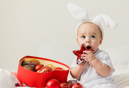 Christmas Baby in Santa Hat Child playing with baubles. Present Gift Box over Holiday Lights background and Merry Christmas