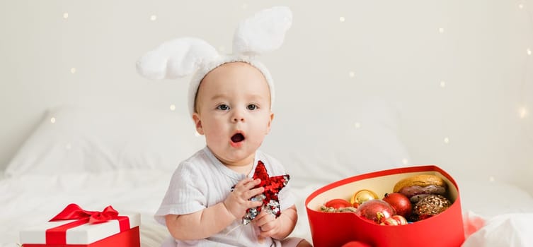 Christmas Baby in Santa Hat Child playing with baubles. Present Gift Box over Holiday Lights background and Merry Christmas