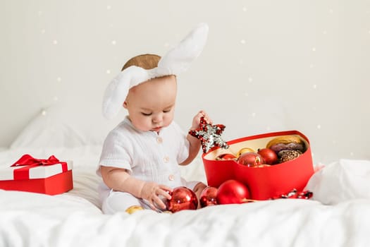 Christmas Baby in Santa Hat Child playing with baubles. Present Gift Box over Holiday Lights background and Merry Christmas