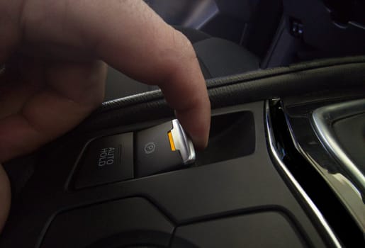 Driver pulling the electric parking brake of his car. Yellow color light indicating brake activation in progress